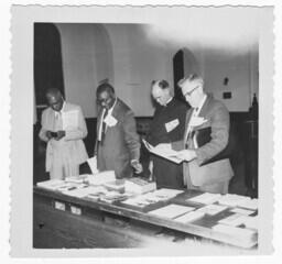 Four Unidentified Men Standing Around Table, February 18, 1958