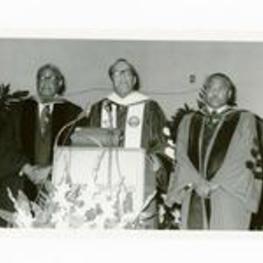 President Hugh Gloster speaking at podium with Dr. E.B. Williams and Dr. E.A. Jones. Written on verso: (l-R) Dr. E.B. Williams, Dr. Gloster, and Dr. E.A. Jones Commencement 1976.