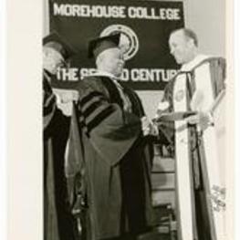 Hugh Morris Gloster shakes hands with a man wearing regalia. On sign in background-Morehouse College, The Second Century.