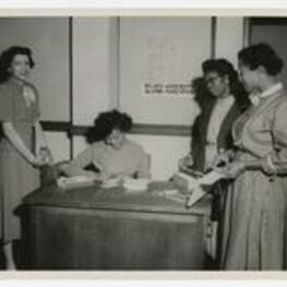 Women stand beside a desk with a sign reading "Atlanta University, Alumni Association".