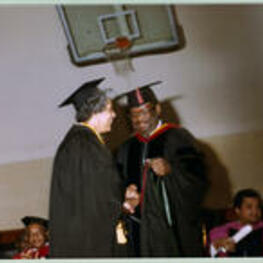 An unidentified graduate shakes James Costen's hand while she receives a red hood.