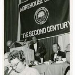View of man standing at a podium, banner in background "Morehouse College, 'The Second Century' ."