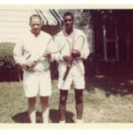 John H. Wheeler stands outside of a house with an unidentified man dressed in tennis gear, holding tennis rackets.