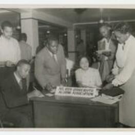 Women and men stand beside a desk with a sign reading"Atlanta University, Alumni Association".