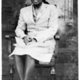 Protrait of an unidentified woman sitting in a chair with her legs crossed in front of a backdrop.