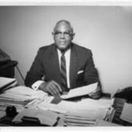 G. Cletus Birchette sits at a desk. Written on verso: Mr. G. Cletus Birchette, Director of Fiscal Affairs, December 1968