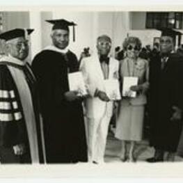 Indoor group portrait of Ossie Davis, Ruby Dee, Dr. Robert Threatt, and George A. Sewell, other man wearing graduation regalia, holding books.