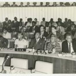 Edward A. Jones and others sit at a long table with with microphones. The sign on the table reads U.S.A.