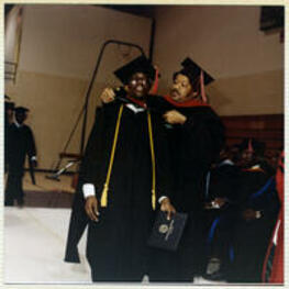 An unidentified man places a red hood on a graduate as he crosses the stage.