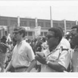 Two unidentified members of the press are shown in the foreground while Coretta Scott King and Leonard Woodcock are shown marching in the background. Written on accompanying document: Mrs. Coretta King and Mr. Woodcock -who replaced Walter Reuther.