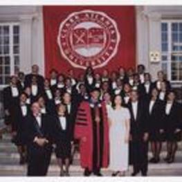 Thomas W. Cole, Jr. poses with a group of men and women, wearing suits with bow ties, on stairs under a banner "Clark Atlanta University."