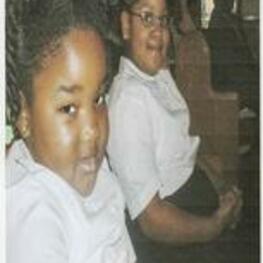 Two unidentified African-American girls wearing white button down shirts sit together in a pew.