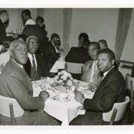 Group portrait of four men seated at a dining table.