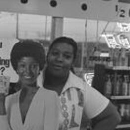 An unidentified woman stands beside an advertising cutout in a liquor store.
