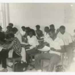 Indoor view of young men and women in classroom seated at desks.