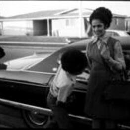 An unidentified boy and woman stand next to a Cadillac car.