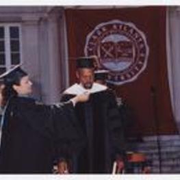 A man receives a graduation hood from a woman on stage at commencement.