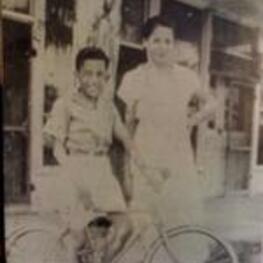 Esther Hubert Griffin stands outside of a store with a young man on a bicycle.