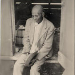 An older man sits in the entry of a storage building. Marked "Grandaddy".