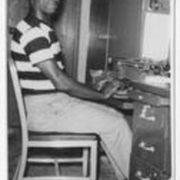 An unidentified man seated at a desk with a typewriter.