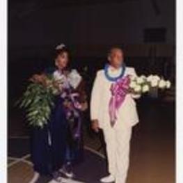 View of man and woman holding bouquets of flowers. Written on verso: "Miss Morris Brown College, Julliette Burgess + Father, Mr. Burgess, Nov. 1987; L to R. Juliette Burgess, Norris Burgess".
