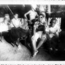 A young Ruby D. Smith sits in a chair and poses with a group of people.