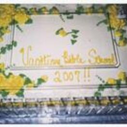 A cake with white icing, decorated with yellow flowers. The inscription on the cake reads Vacation Bible School 2007. Written on verso: Shy Temple Vacation Bible School 6-26-2007.