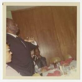 Howard Thurman speaks at a luncheon while men and women sit at the table.