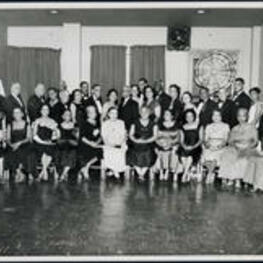A group portrait of men and women at a Sigma Pi Phi Fraternity event. Written on verso: Atlanta's Kappa Boule Observed Annual Ladies Night for 1958. Extraneous note: Dr. Manley (2nd row left), Dr. Rufus Clement (2nd row second from left), Mr. and Mrs Brazeal (back row center), Whitney Young (2nd row fourth from right), Dr. Clarence Bacote (back row behind Rufus Clement).