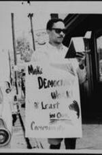 Atlanta University student John Gibson protests outside of a business with a sign that reads: "Make Democracy Work! At Least in Our Community".