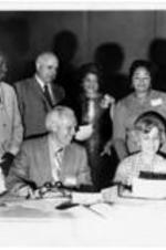 Robert E. Penn (left) gathers with an unidentified group around a table covered with papers. Written on verso: "May 1972"