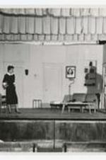 View of man and woman on stage, view of living room furniture.