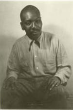 Portrait of Jacob Lawrence sitting with his hands on his knees.