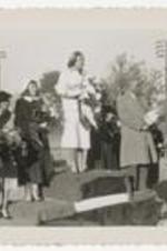 Outdoor view of women on a podium with a man holding a crown on a football field.