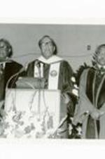 President Hugh Gloster speaking at podium with Dr. E.B. Williams and Dr. E.A. Jones. Written on verso: (l-R) Dr. E.B. Williams, Dr. Gloster, and Dr. E.A. Jones Commencement 1976.
