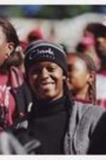 A young woman, wearing a beanie hat "Clark Atlanta", smiles surrounded by other men and women.