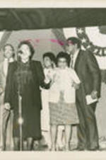 Dorothy Cotton and an unidentified man stand at microphones on a stage with several individuals behind them, including Reverend James Orange (second from right).