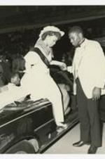 Indoor view of man assisting woman out of convertible. Written on verso: "Mr. David Kinchen assists Miss MBC- Michelle Patmon out of her limousine 1984-85".