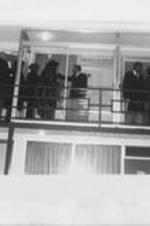 A group of people are shown standing on the walkway of the second floor of the Lorraine Motel. A banner memorializing Martin Luther King, Jr. can be seen displayed through a window.