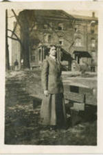 A woman poses next to a bench in front of a large building.