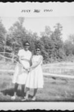 Two unidentified women wearing white dresses hold a large landing net.