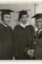 James P. Brawley, holding a 1955 yearbook, poses with two graduates at commencement.