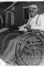 An elderly man sits in a wheelchair and reads a paper outside the Happy Haven Nursing Home, now named Sadie G. Mays Health and Rehabilitation Center.