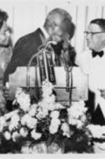 Jackie and Rachel Robinson are shown standing behind a podium with Branch Rickey at the Testimonial Dinner held for Robinson at the Waldorf Astoria in New York City on July 20, 1962.