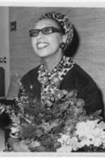 Josephine Baker holding a bouqet of flowers. Written on verso: New York Bureau. Josephine Baker arrives in U.S. New York: Holding a bouquet of Flowers, American-born Negro singer smiles as she answers newsmen's questions following her arrival at Idlewild Airport here, Feb. 10th. Miss Baker said that attacks she had made on racial conditions in the U.S. had been "exaggerated." She is scheduled to make appearances in New York, Chicago and Las Vegas. 2-10-60 JL