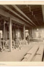 Interior of the machine room with students standing near equipment. The machine room was located on the first floor and included steam powered saws and grinders. Written on recto: Machine room.