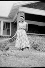 An unidentified woman waters the yard with a hose in front of a house.