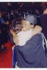 Two graduates embrace at commencement.