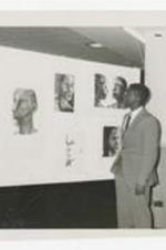 A young man looks at wall of portraits.