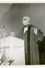 An unidentified man wearing regalia, delivers a speech at a podium.